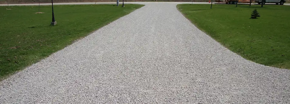 A gravel driveway extends through a green, grassy yard towards the street.