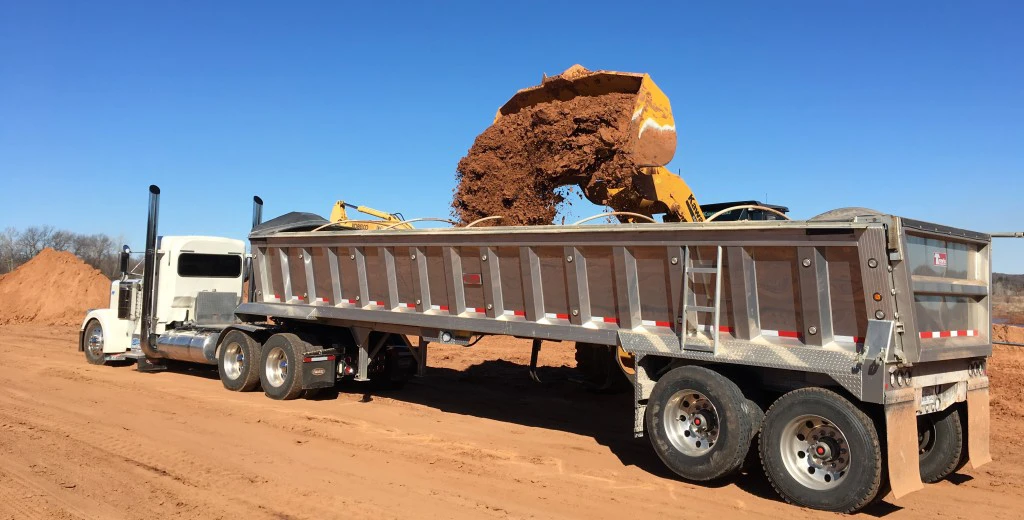 A large truck is loaded with sand using earth-moving equipment.